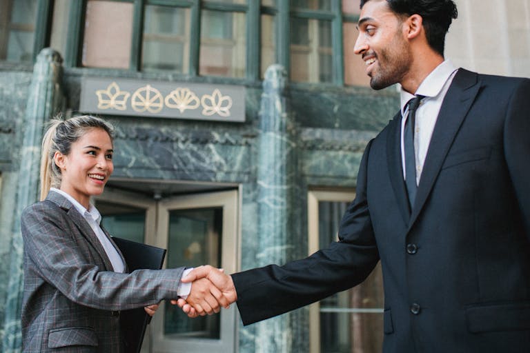 Two business professionals shaking hands confidently outside a modern building.